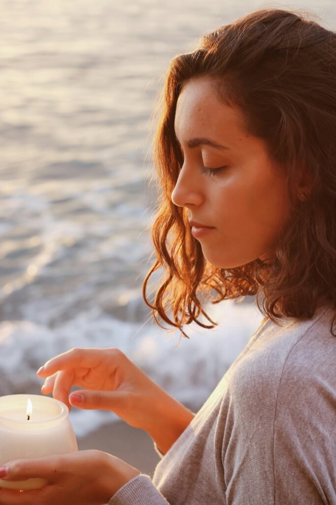 Young woman in a quiet moment holding a candle by the ocean at sunset